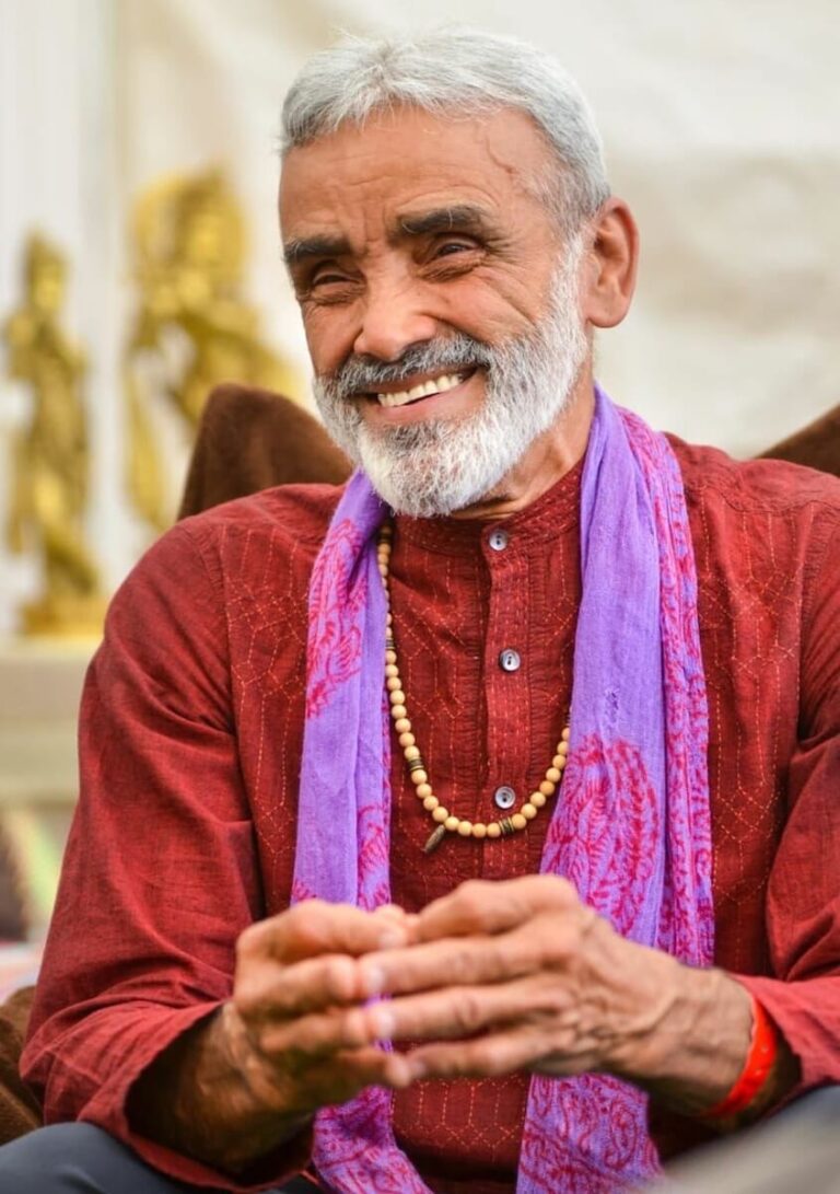 Sri Dharma in red shirts and purple shawl with smile on his face.